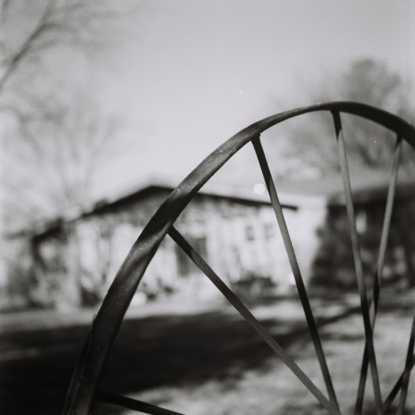 The wheel of a hay rake with my house in the morning.
